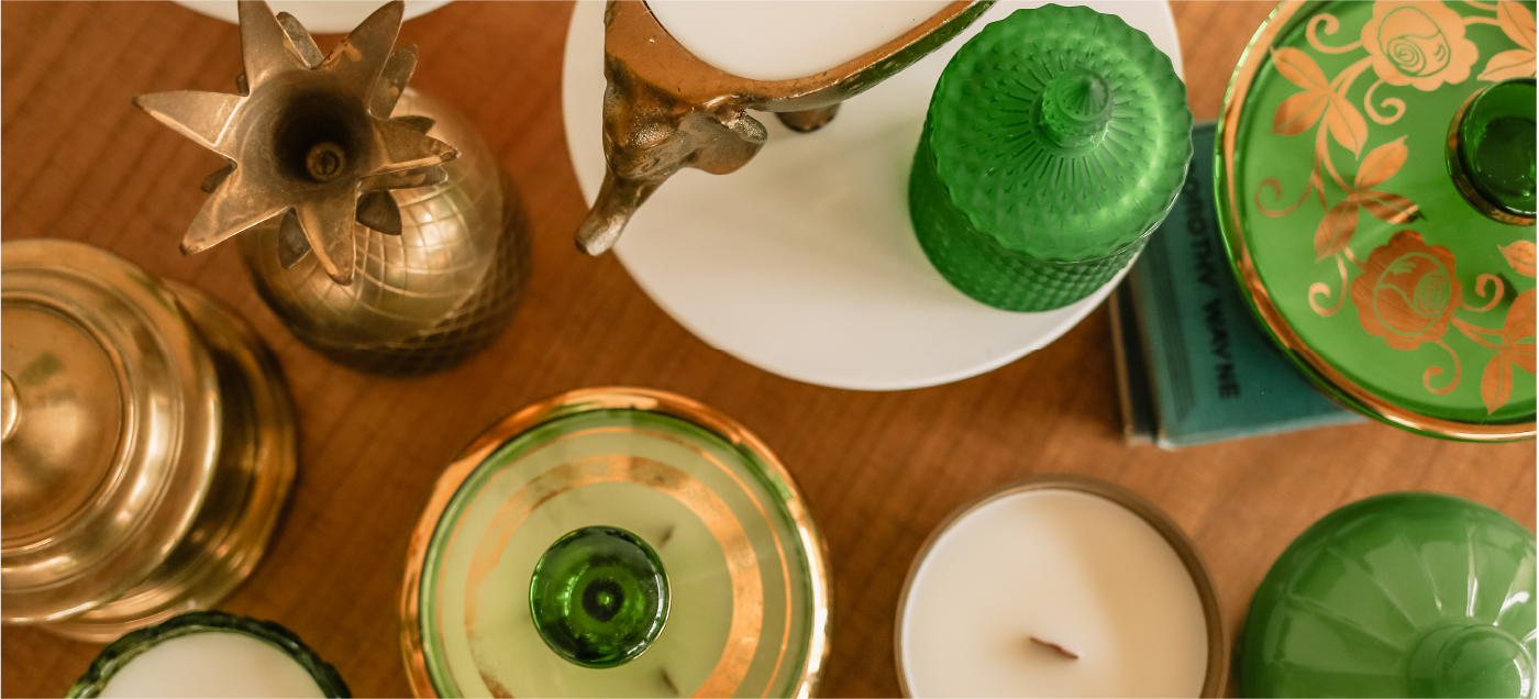 Aerial view of an assortment of candles in bronze and green containers on a brown wooden tabletop.